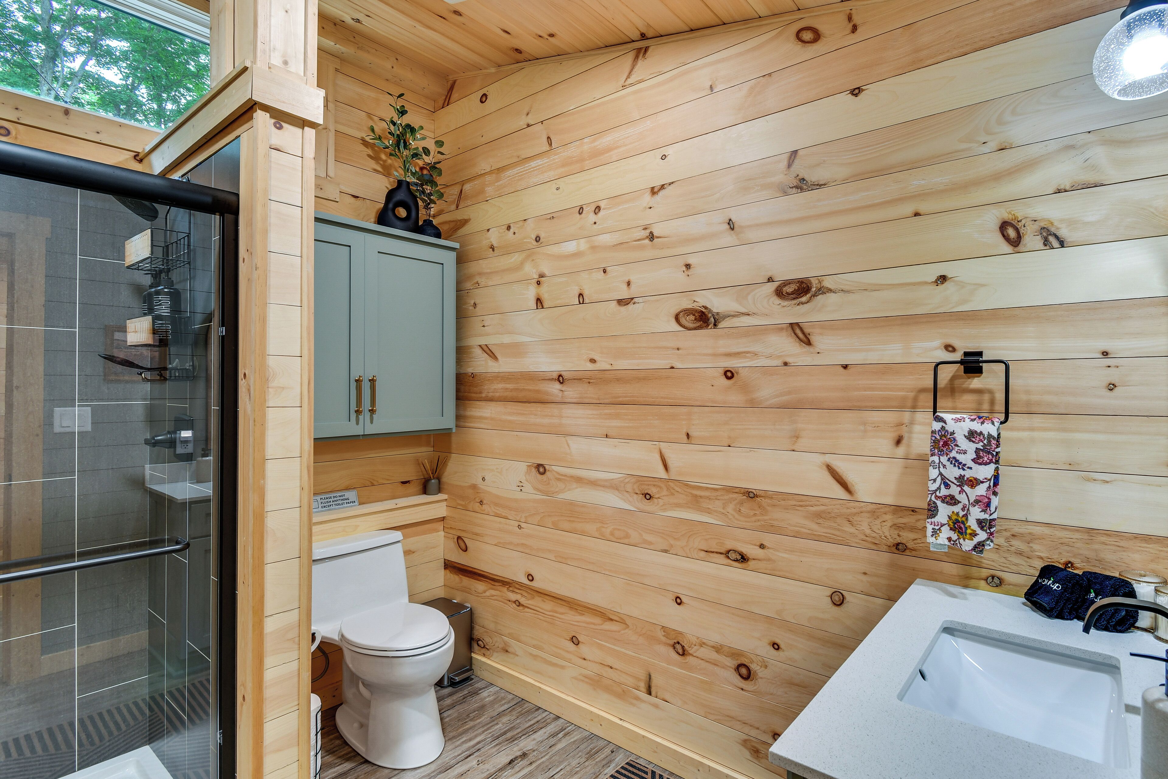 Ein Badezimmer mit Holzwandverkleidung, Toilette, Waschbecken und Duschbereich.