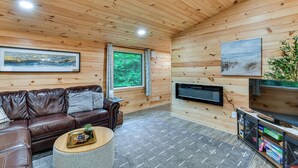 A wooden-paneled room with a leather sofa, a flat-screen TV, and a fireplace. - Explore Lakes & Beaches! Creekside Glen Arbor Home (Glen Arbor)
