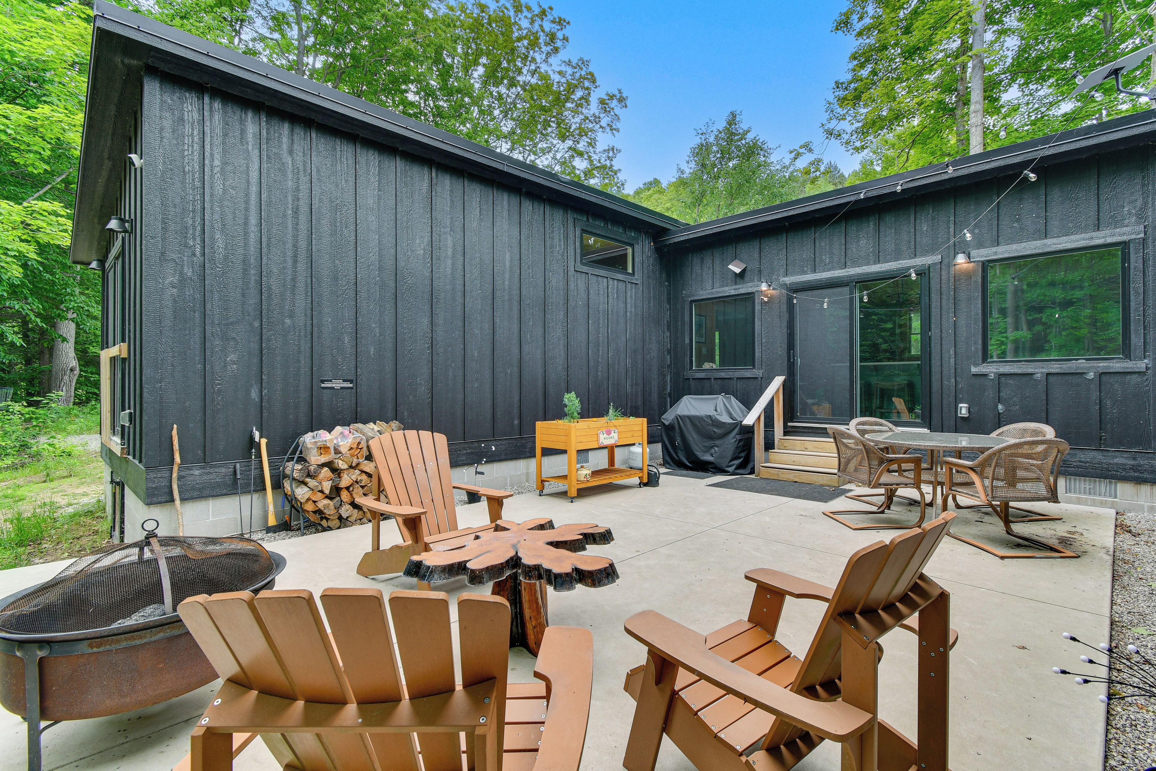 An outdoor patio with wooden furniture, a fire pit, and a grill area.