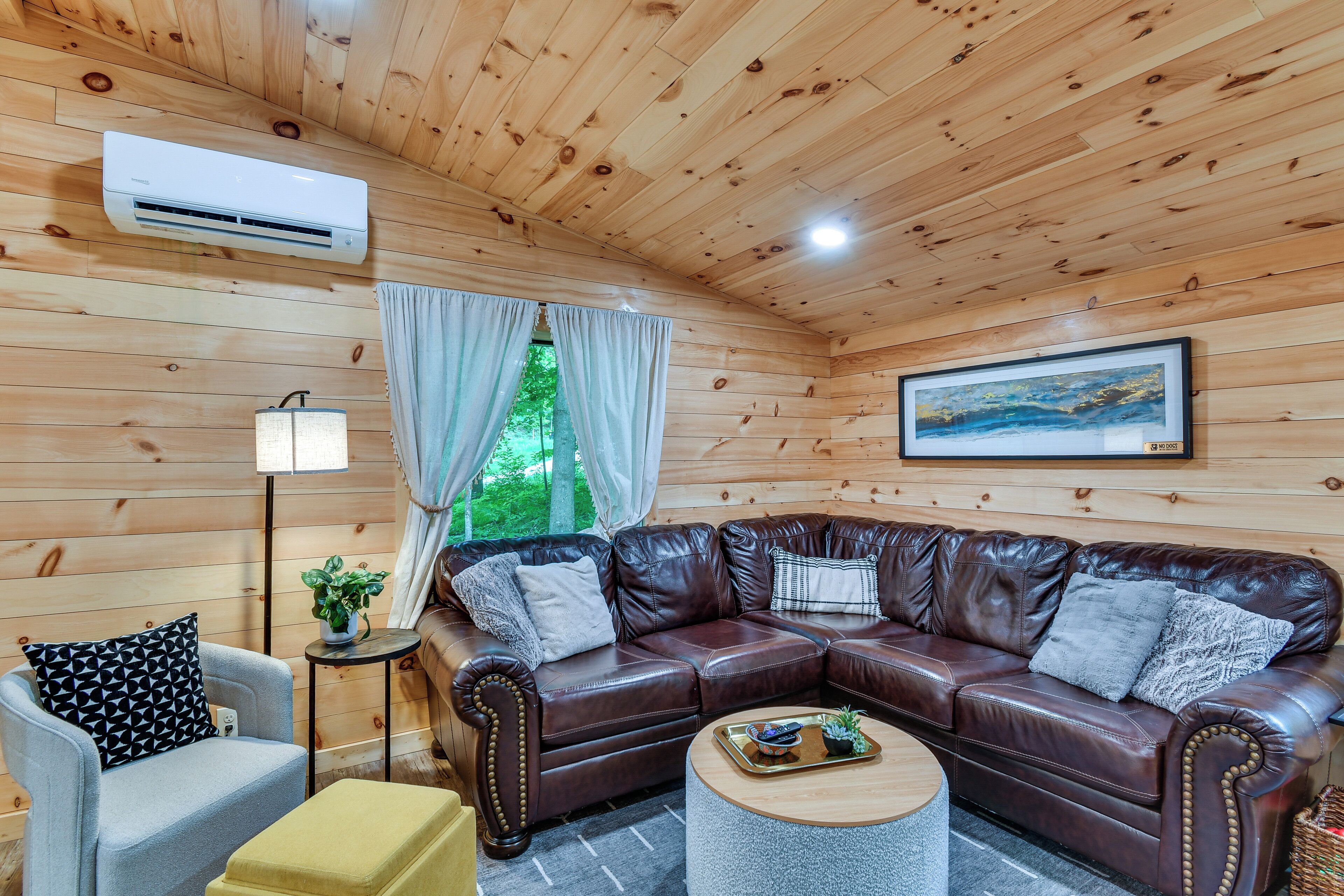 A wooden-paneled room with a leather sectional sofa, a small armchair, a round coffee table, and a floor lamp.