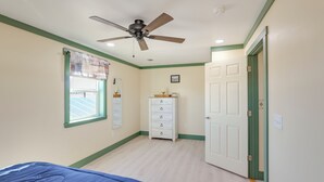 A bedroom with a bed, a ceiling fan, a dresser, and a door.