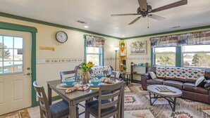 A dining area with a table set for four, a sofa, a ceiling fan, and a view of the outdoors.