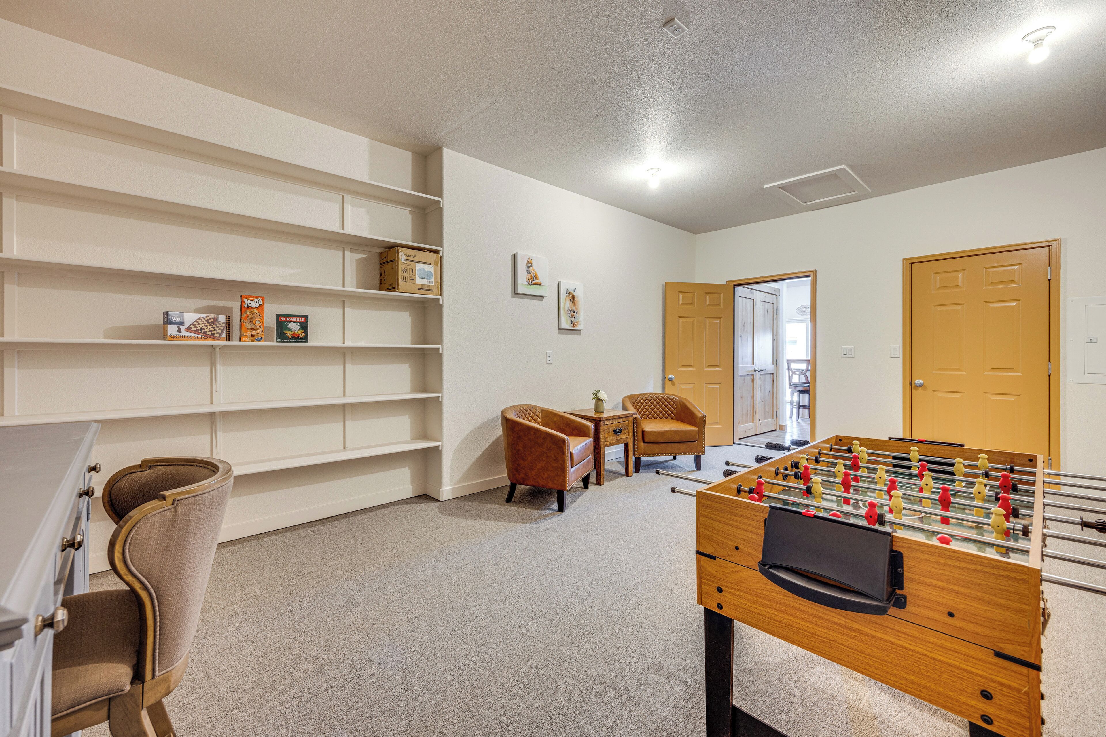 A room with a foosball table, two armchairs, a bookshelf, and a door.