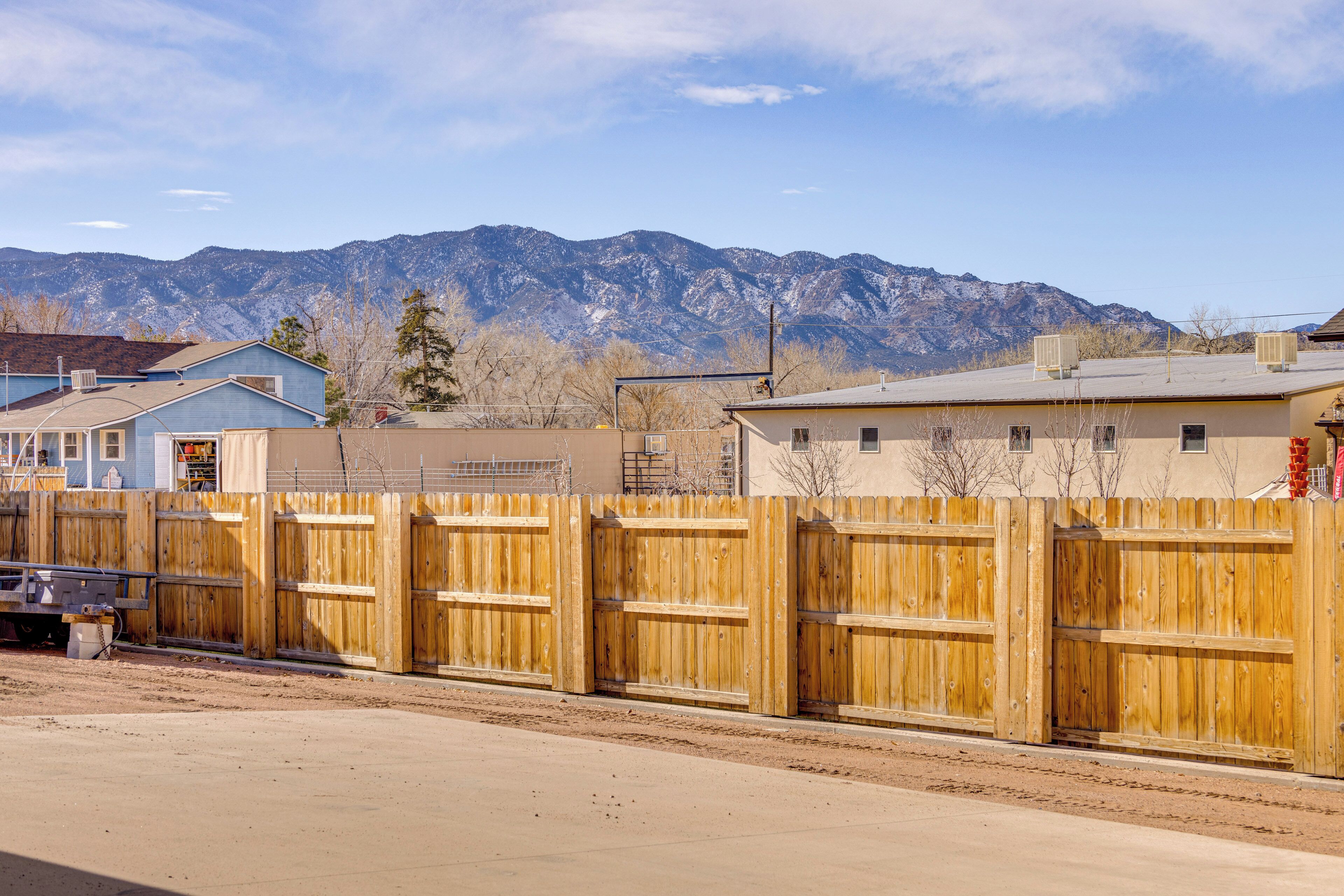 A fenced area with a mountain backdrop, a building with a flat roof, and a clear sky.