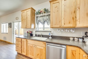 A kitchen with wooden cabinets, a stainless steel dishwasher, and a window with curtains.