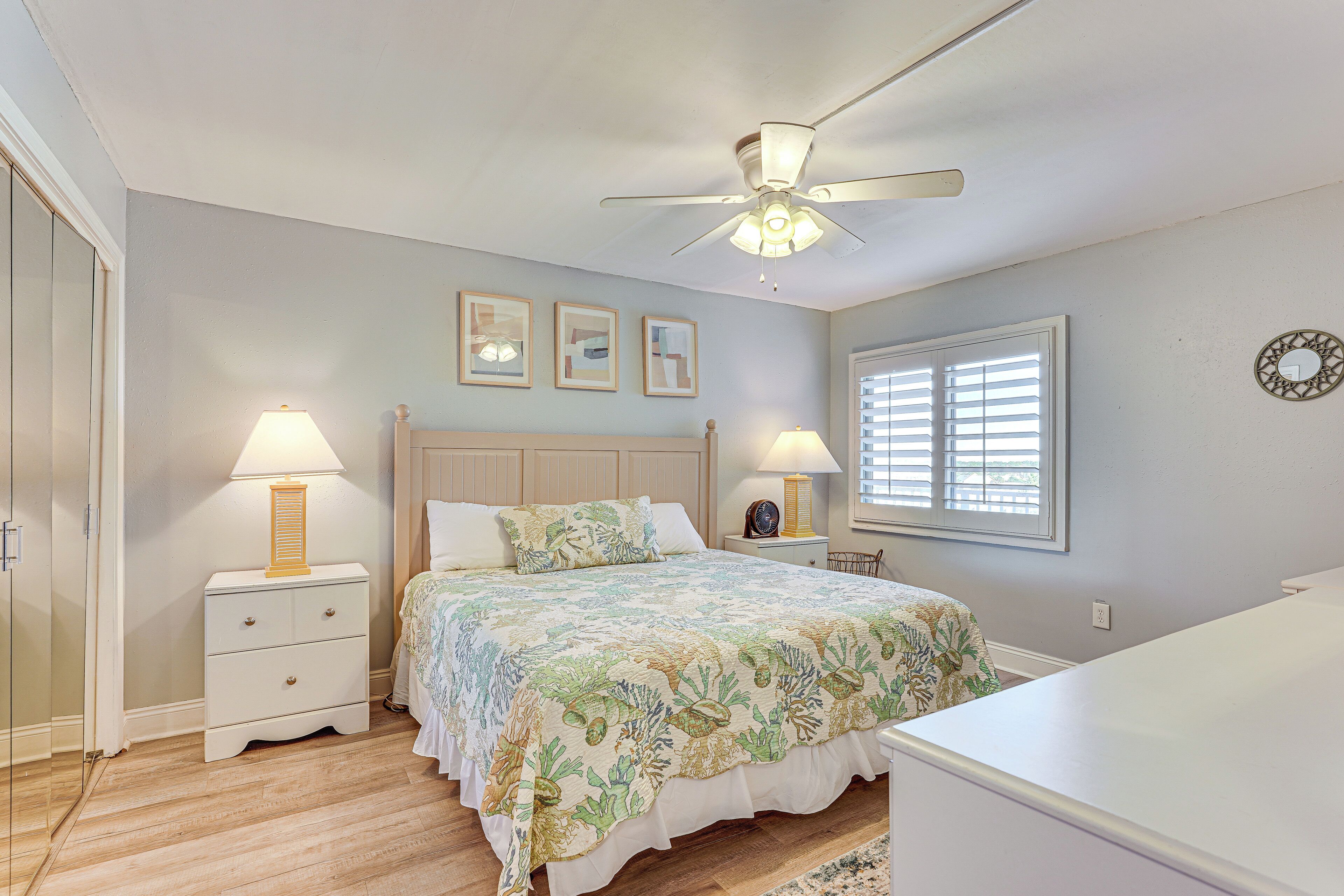 A bedroom with a bed, two bedside tables with lamps, a ceiling fan, and a window with blinds.