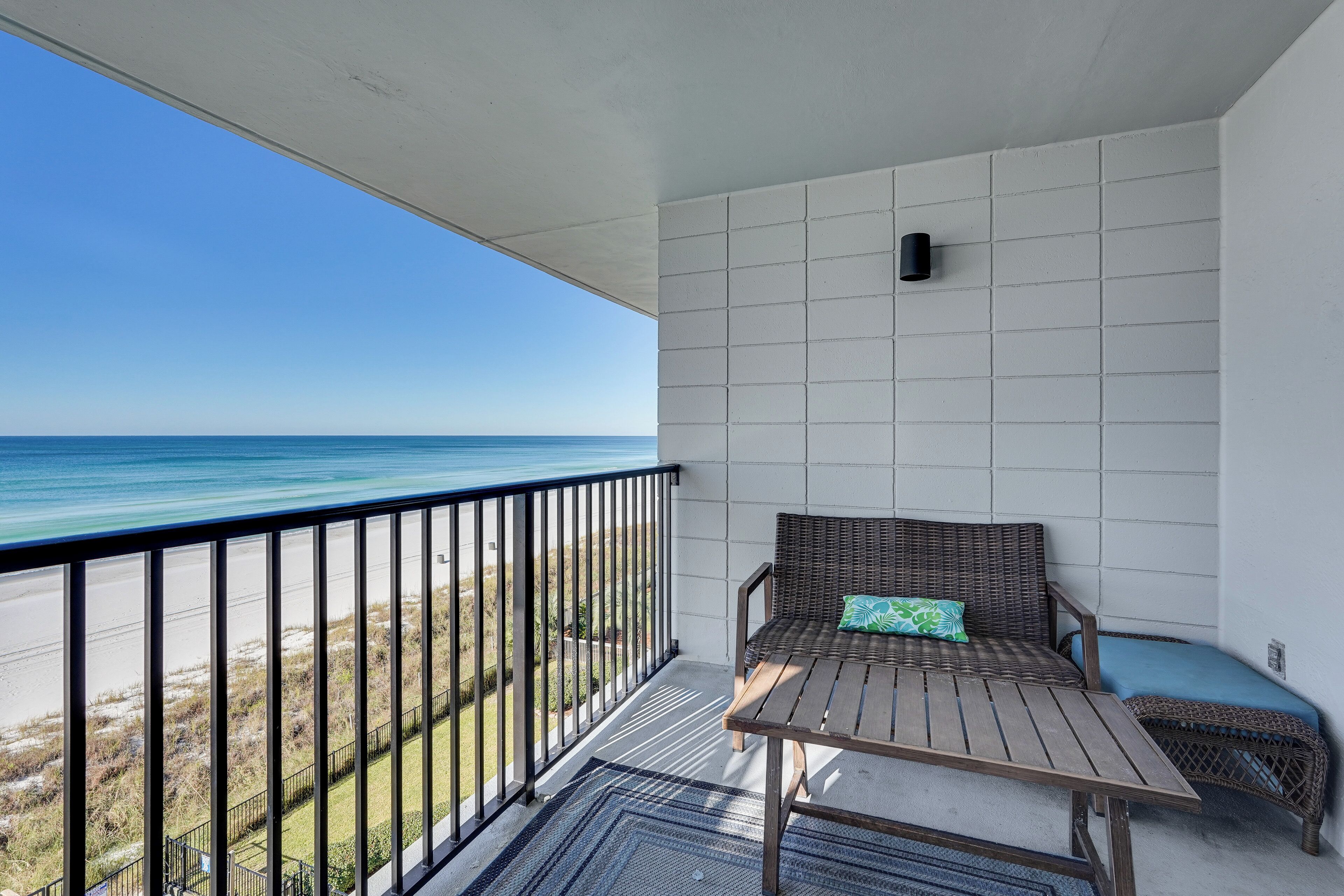 A balcony with a view of the ocean, a wicker sofa with cushions, and a small table.