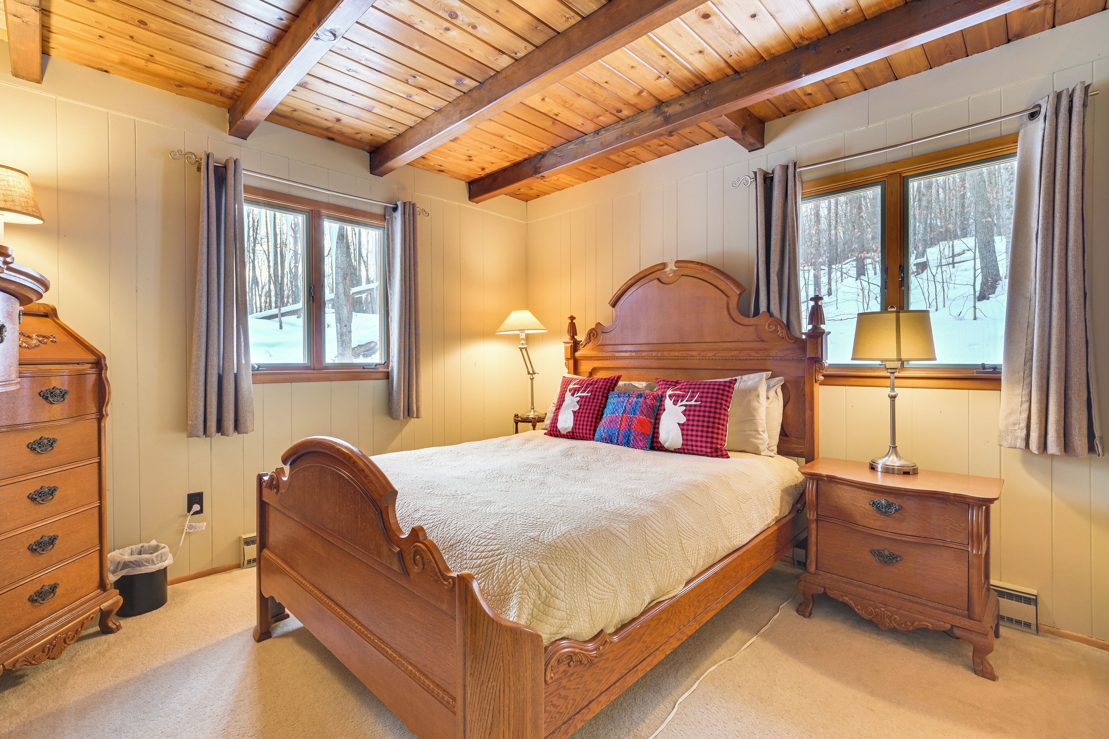 Una cama de madera con colcha, mesitas de noche y una ventana con cortinas.
