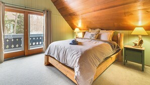 A bedroom with a wooden ceiling, a large bed, two bedside lamps, and a view through a sliding glass door. - 2 Mi to Schuss Mountain: Cozy Cabin w/ Deck (Bellaire)