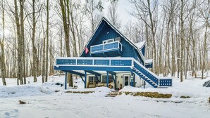 A blue cabin with a balcony and a staircase, surrounded by snow and trees. - 2 Mi to Schuss Mountain: Cozy Cabin w/ Deck (Bellaire)