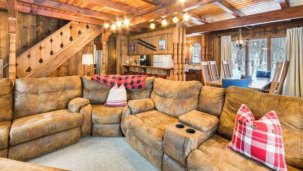 A cozy wooden interior with a large sectional sofa, a staircase, and a dining area. - 2 Mi to Schuss Mountain: Cozy Cabin w/ Deck (Bellaire)