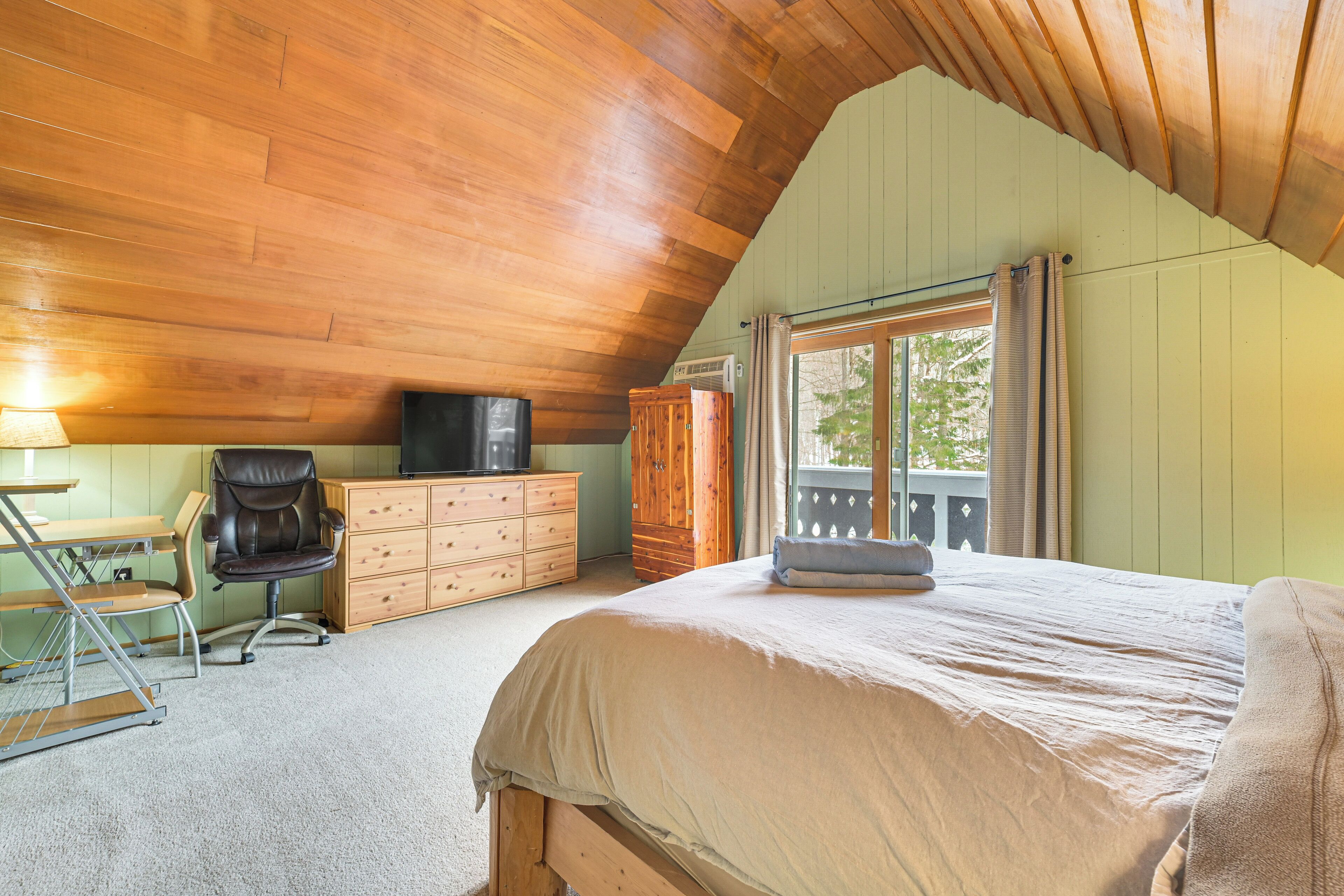 Une chambre avec un plafond en pente, un lit, un bureau avec une chaise, une commode et un téléviseur.