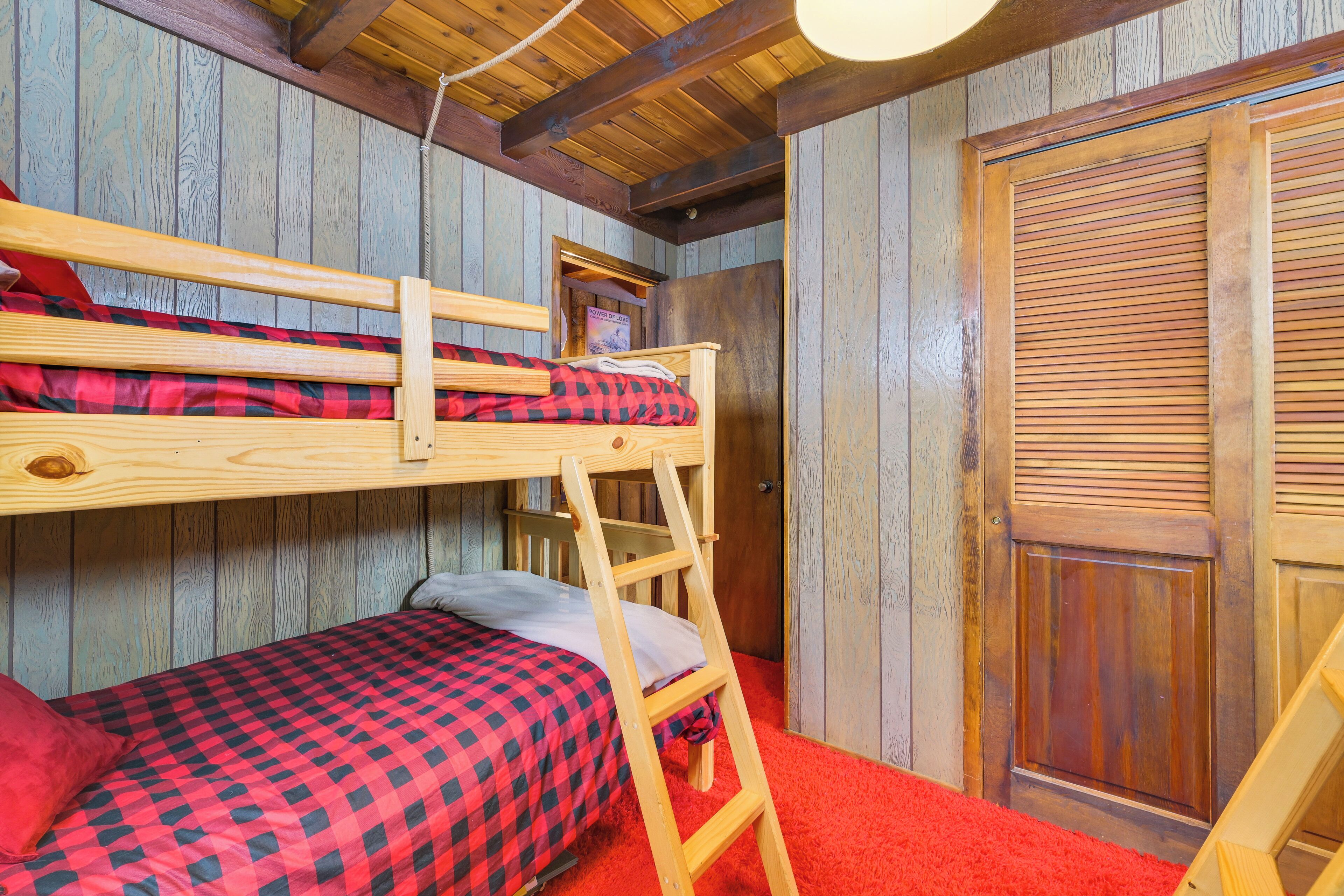 A bunk bed room with a wooden ladder, a door, and a red carpet.