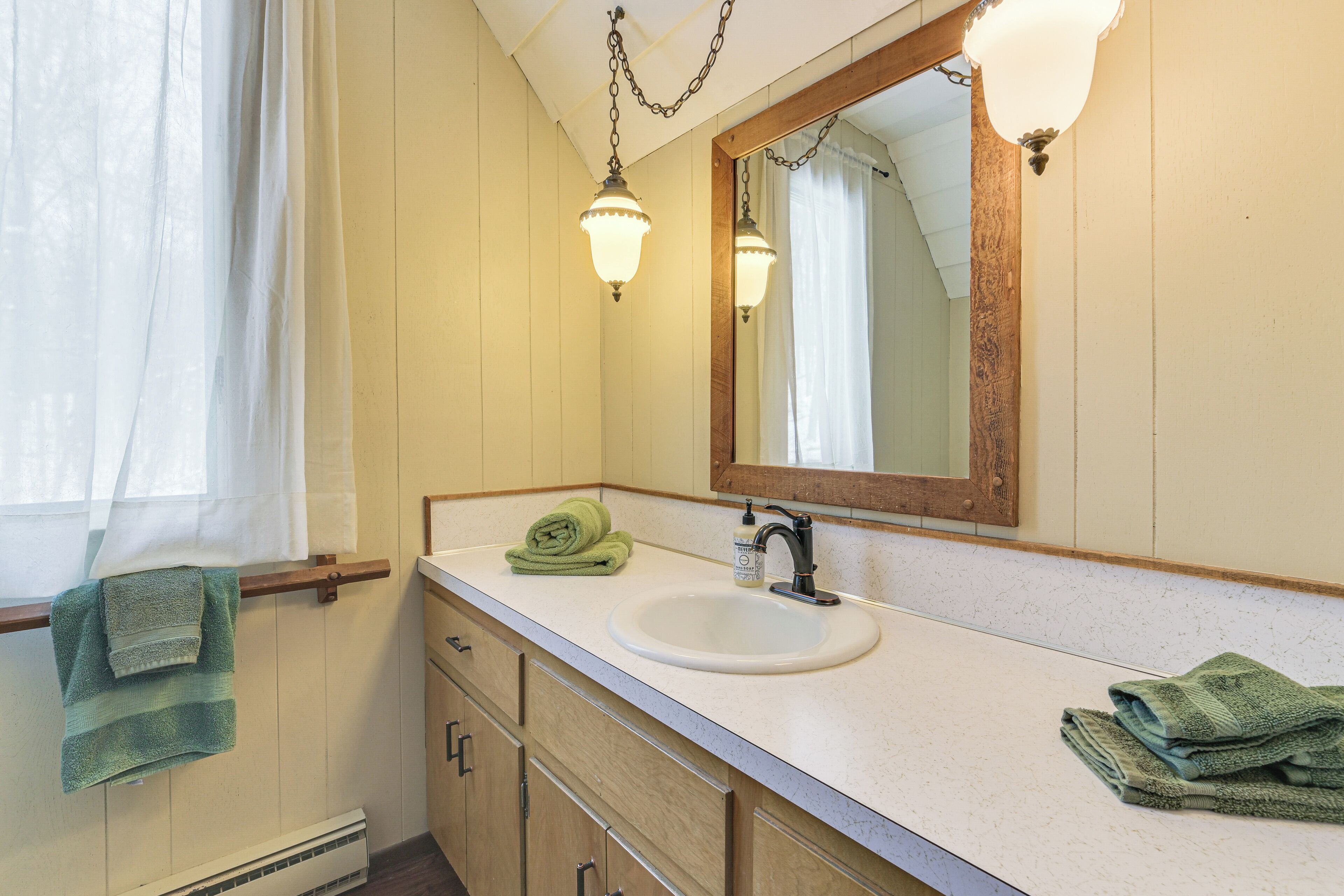 A bathroom with a white sink, wooden cabinets, a mirror, and two wall-mounted lights.