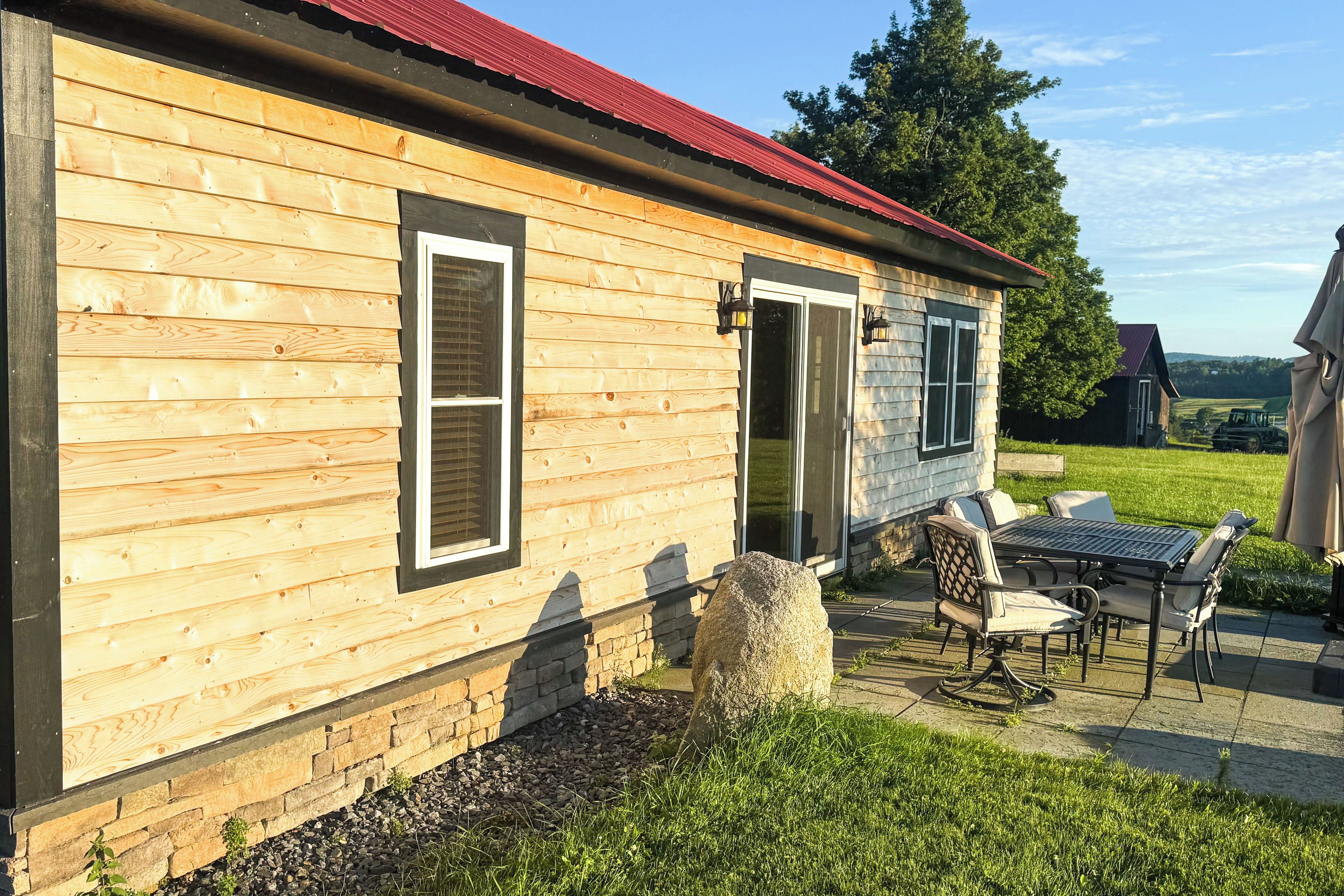 Una cabaña de madera con techo rojo, base de piedra y un patio con mobiliario exterior.