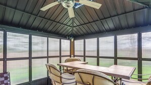 Een overdekt terras met een tafel, stoelen, grote ramen en een plafondventilator.