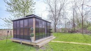 Een modern glazen huis met een houten terras, omringd door een gazon en bomen.