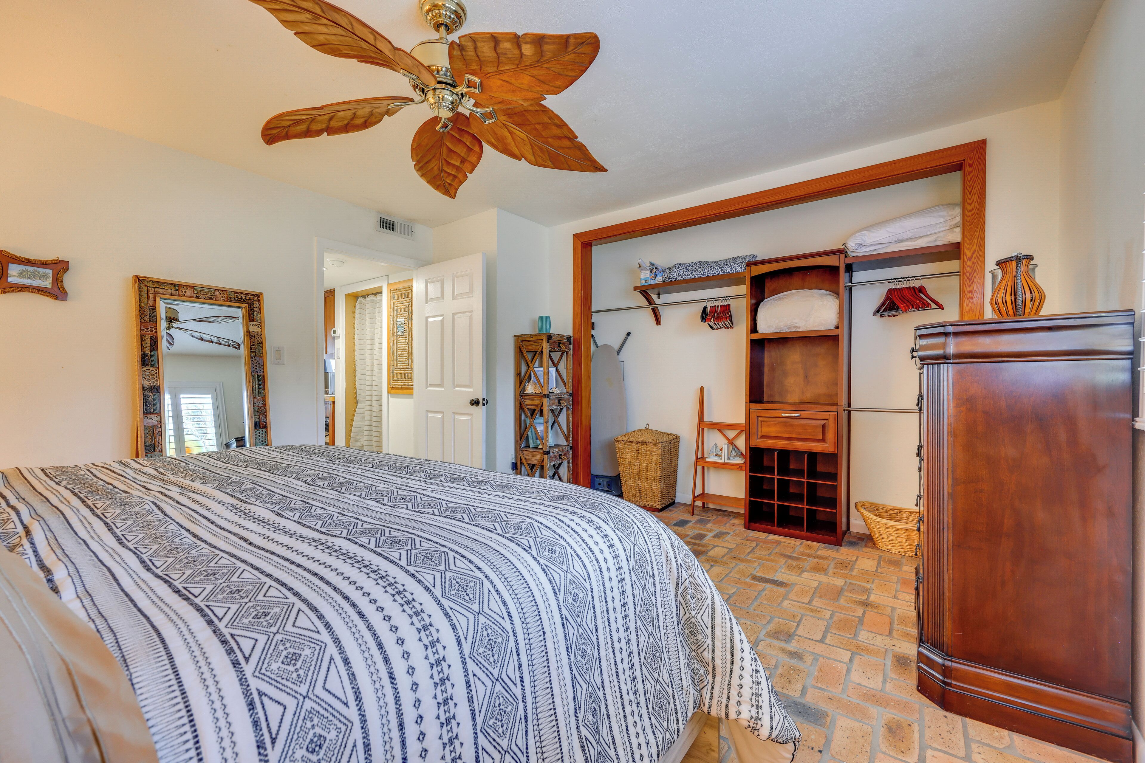 A bedroom with a large bed, a wooden wardrobe, a ceiling fan, and a wardrobe with hanging clothes.