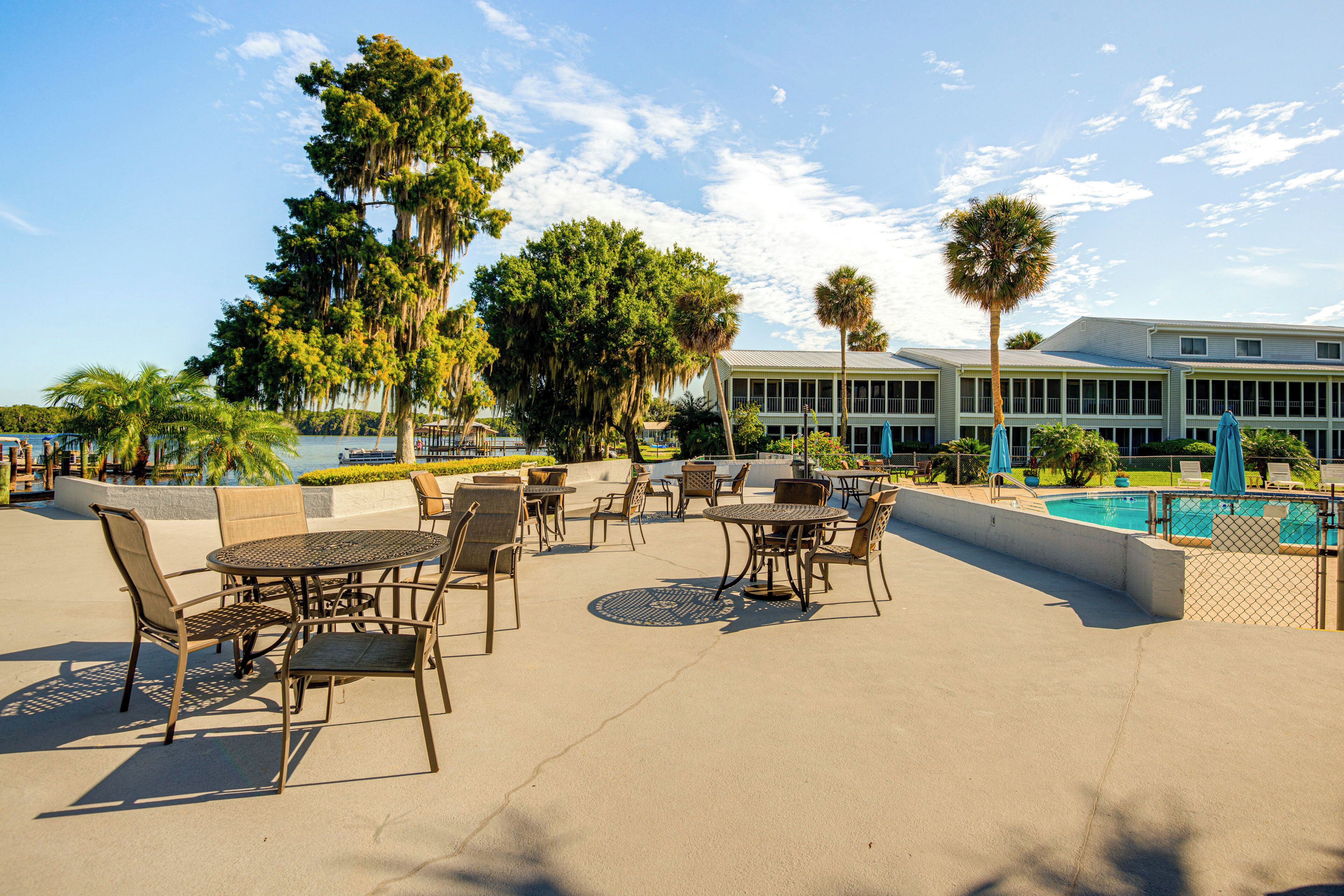 An outdoor patio area with tables and chairs, a pool, and a building in the background.