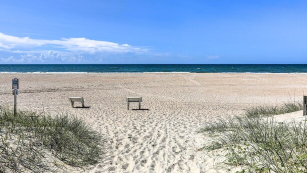 Una playa con dos sillas vacías y un cartel.
