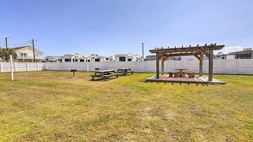 A grassy outdoor area with picnic tables and a wooden pergola.