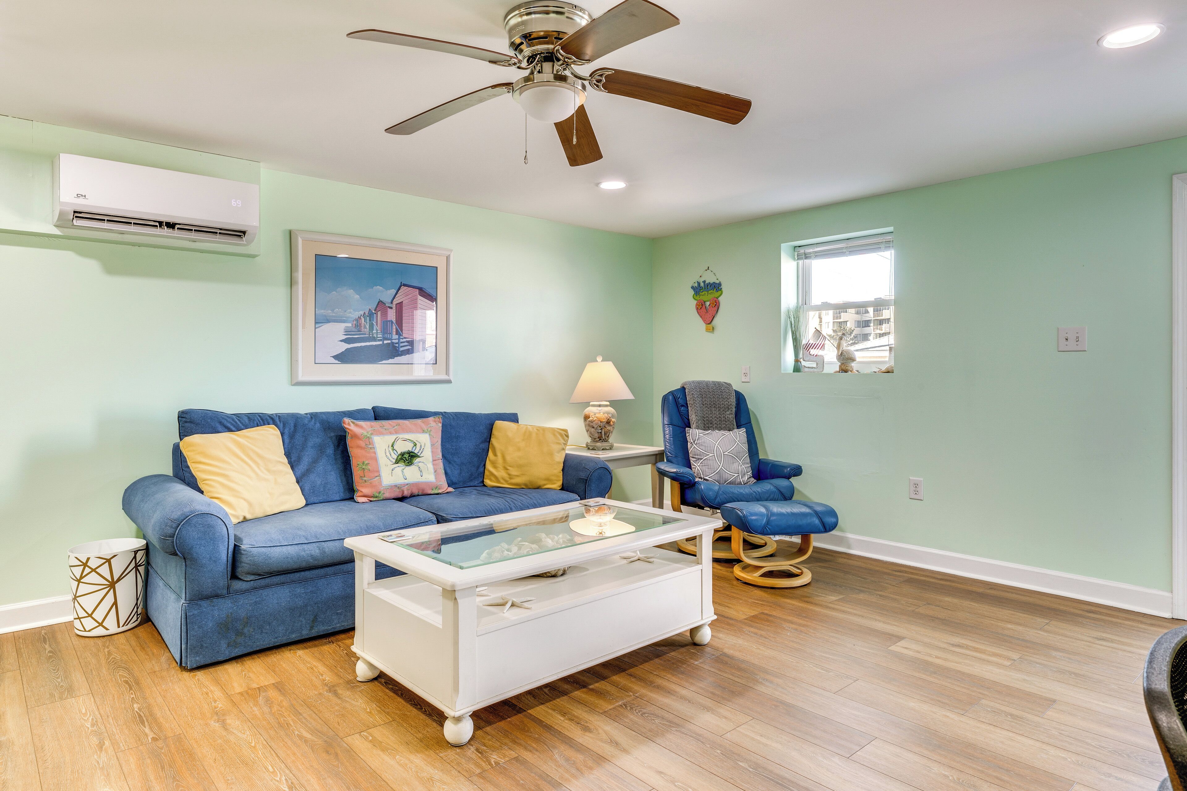 A living room with a blue sofa, a white coffee table, a ceiling fan, and a window with a view.