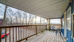 A wooden deck with a railing, two chairs, and a view of a red vehicle and trees in the background. - Rustic Apartment w/ Sunset Views in Elkhart! (Elkhart)