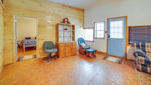 A room with wooden walls, a bed, a wooden cabinet, a rocking chair, a blue armchair, and a plaid sofa. - Rustic Apartment w/ Sunset Views in Elkhart! (Elkhart)