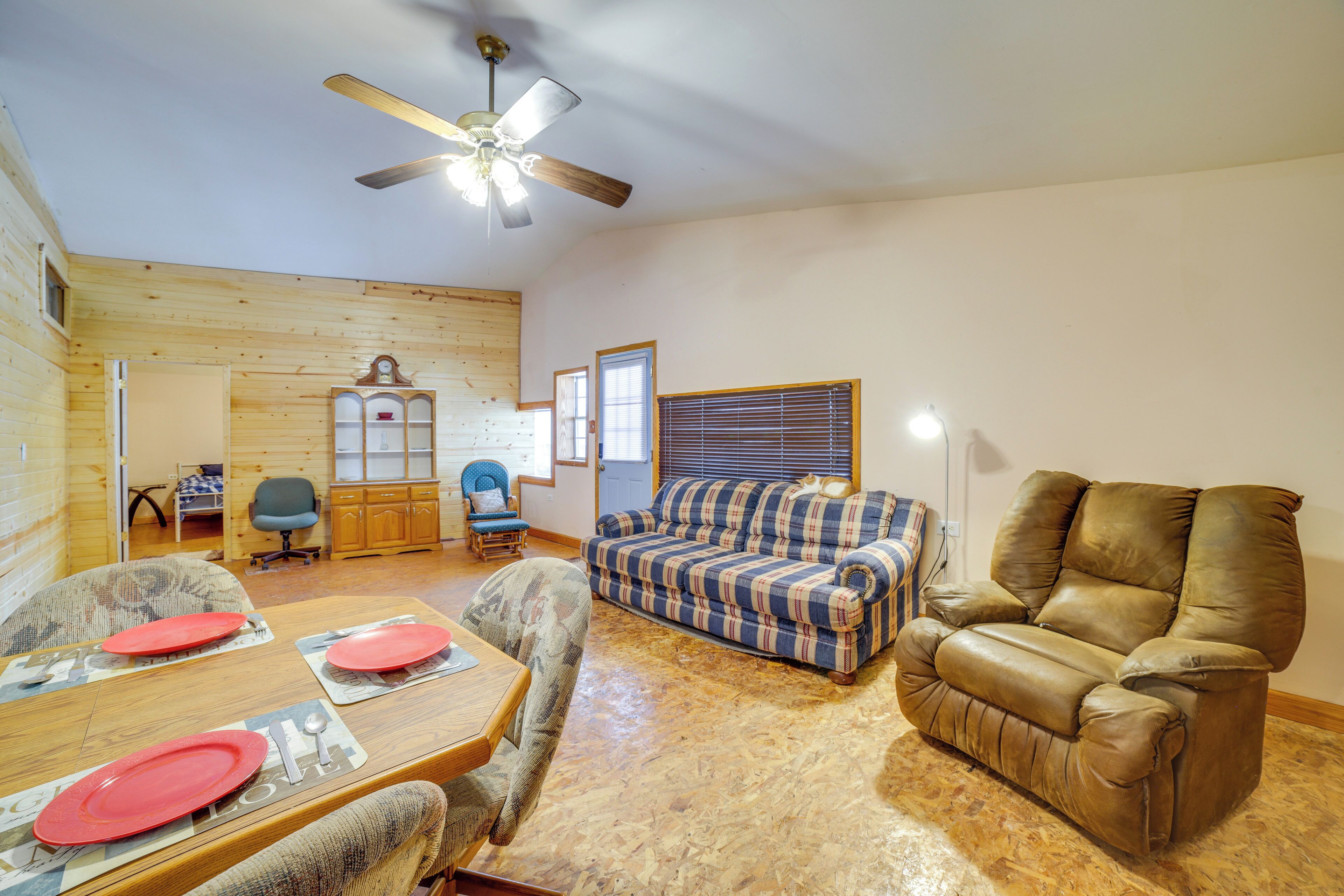 A cozy living room with a wooden floor, a plaid sofa, a leather recliner, and a dining table set for four.