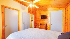 A wooden cabin bedroom with a bed, a ceiling fan, a TV mounted on the wall, and a fireplace. - Rustic Apartment w/ Sunset Views in Elkhart! (Elkhart)