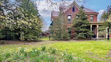 Classic brick home with a gabled roof and covered porch, surrounded by a lush lawn and mature trees.