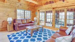 A wooden cabin interior with a leather sofa, a coffee table, and a large window. - Private Boat Ramp & Dock: Kentucky Lake Cabin! (Camden)