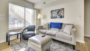 A living room with a grey sofa, a black leather chair, a small table, and a remote control on a beige ottoman. - 15 Mi to Greensboro: Archdale Condo w/ Fireplace (High Point)