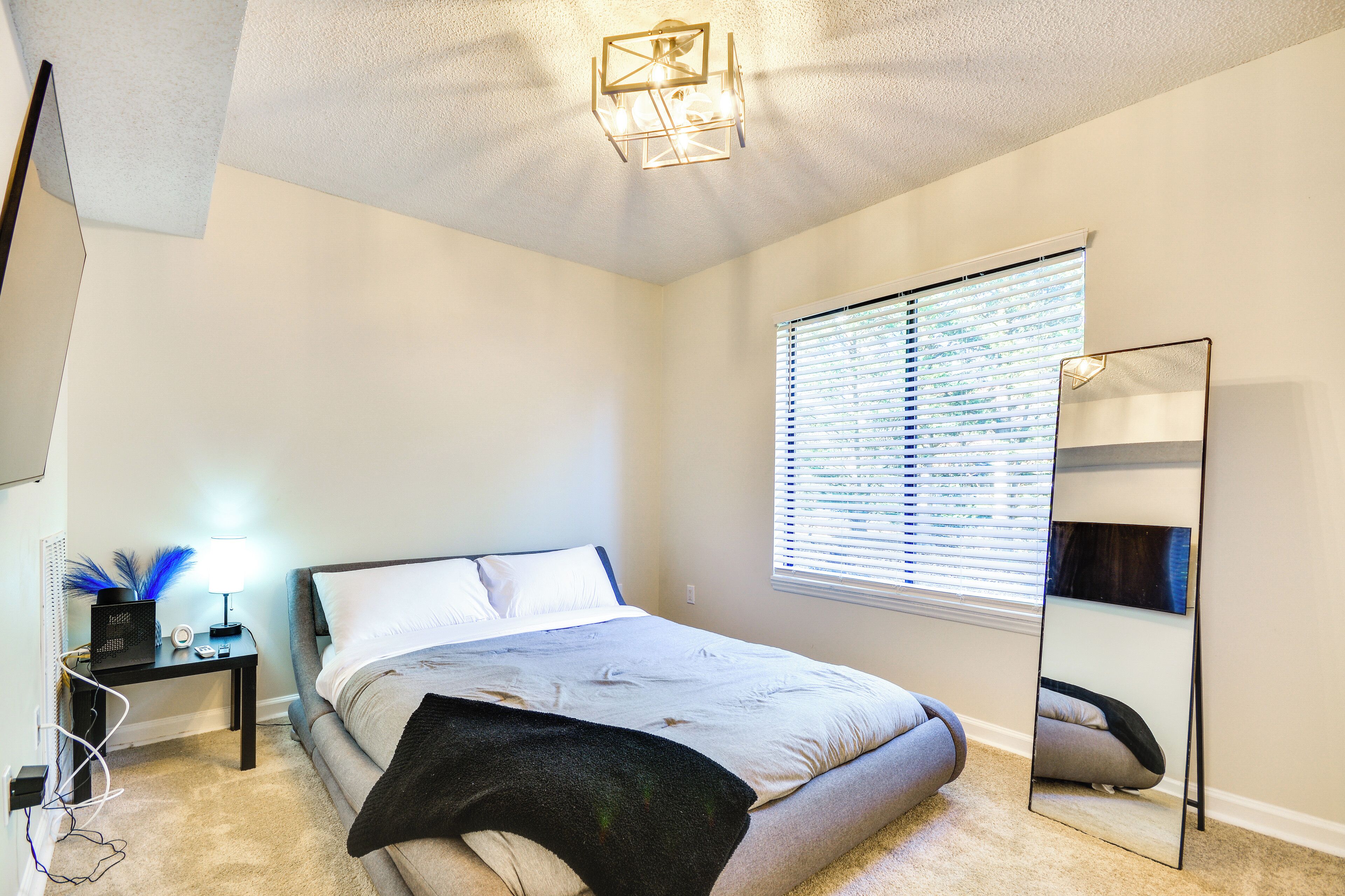 A bedroom with a bed, bedside table, lamp, and a large mirror.