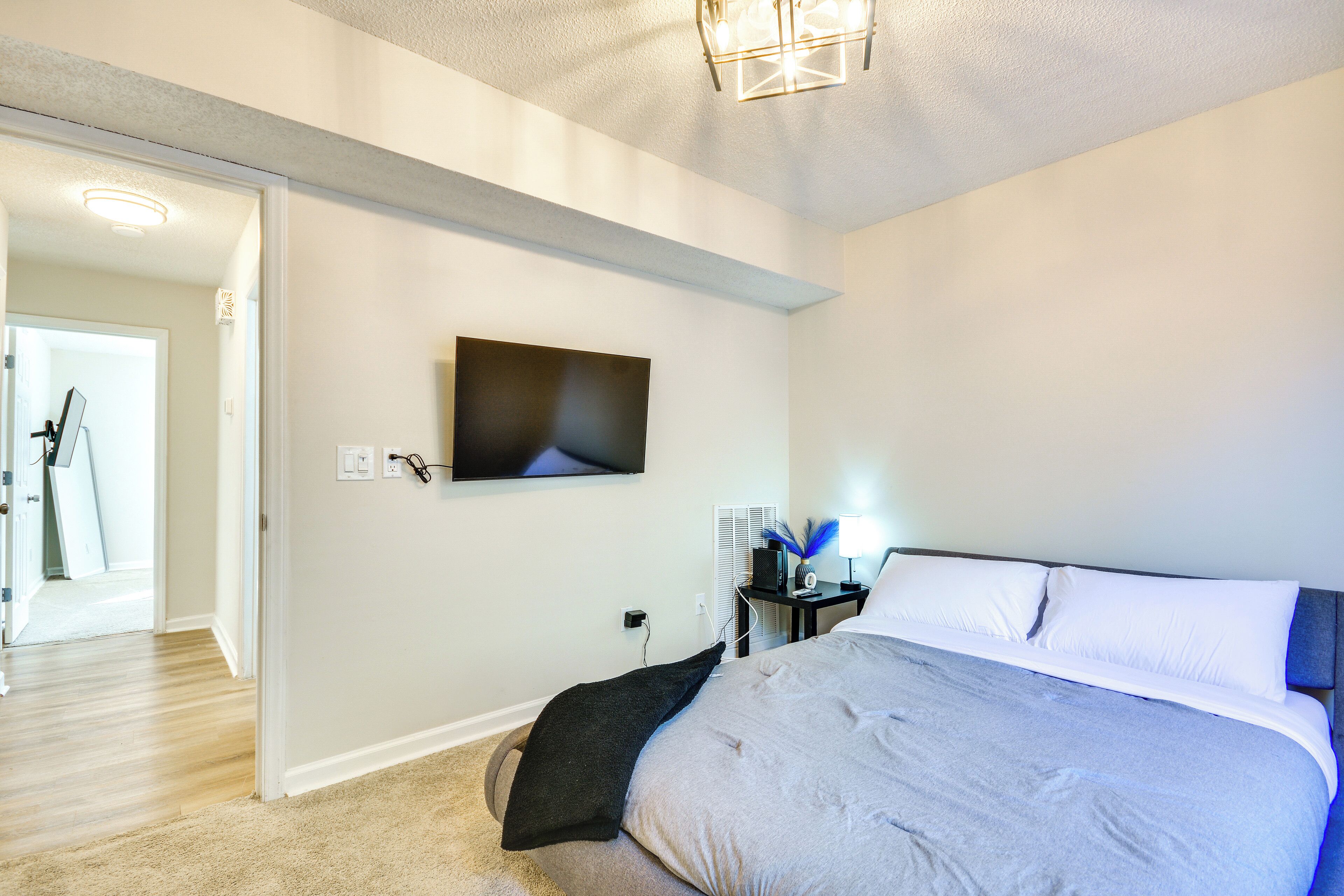 A bedroom with a bed, a flat-screen TV mounted on the wall, and a bedside table with a lamp.
