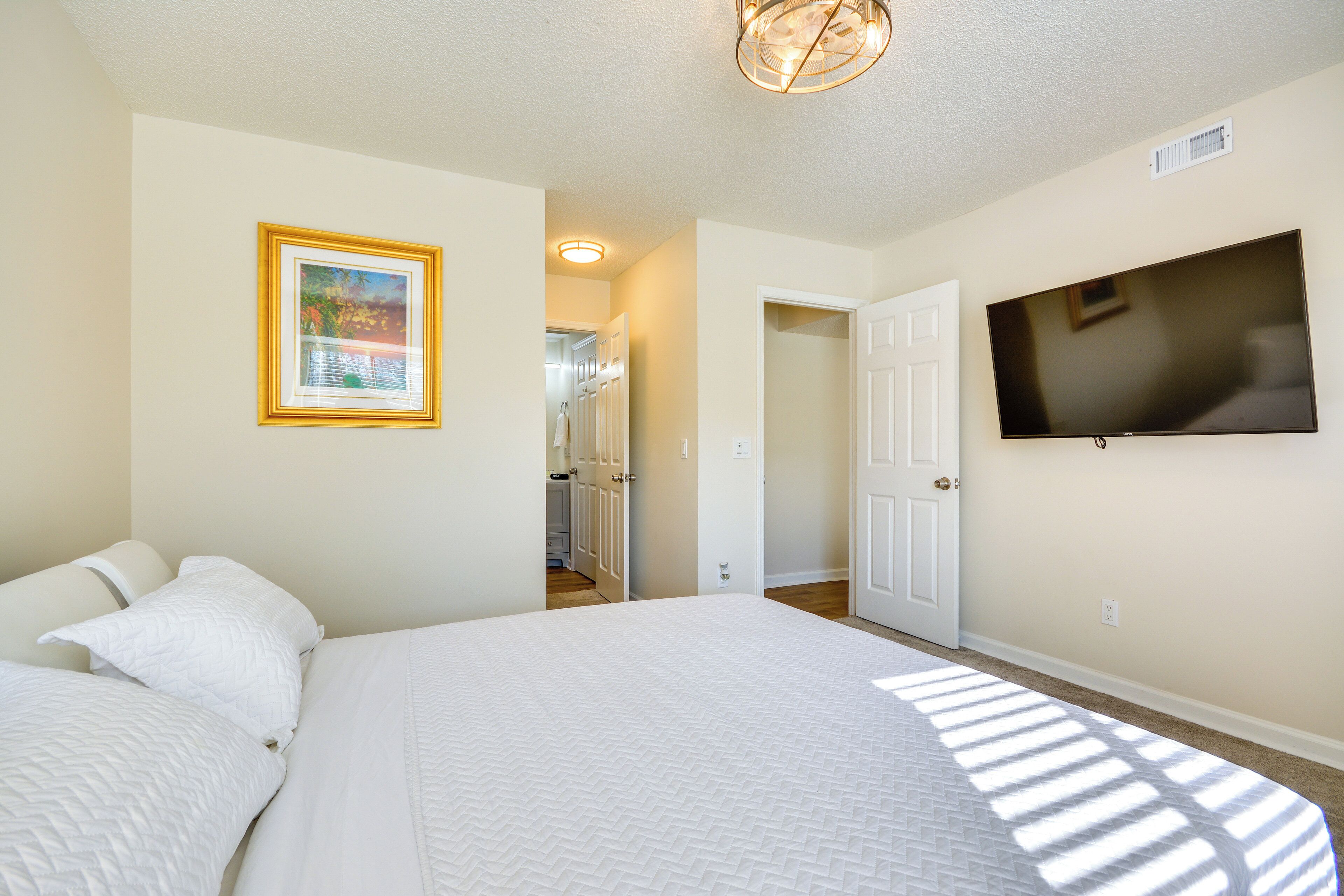 A bedroom with a large bed, a television mounted on the wall, and a door leading to another room.