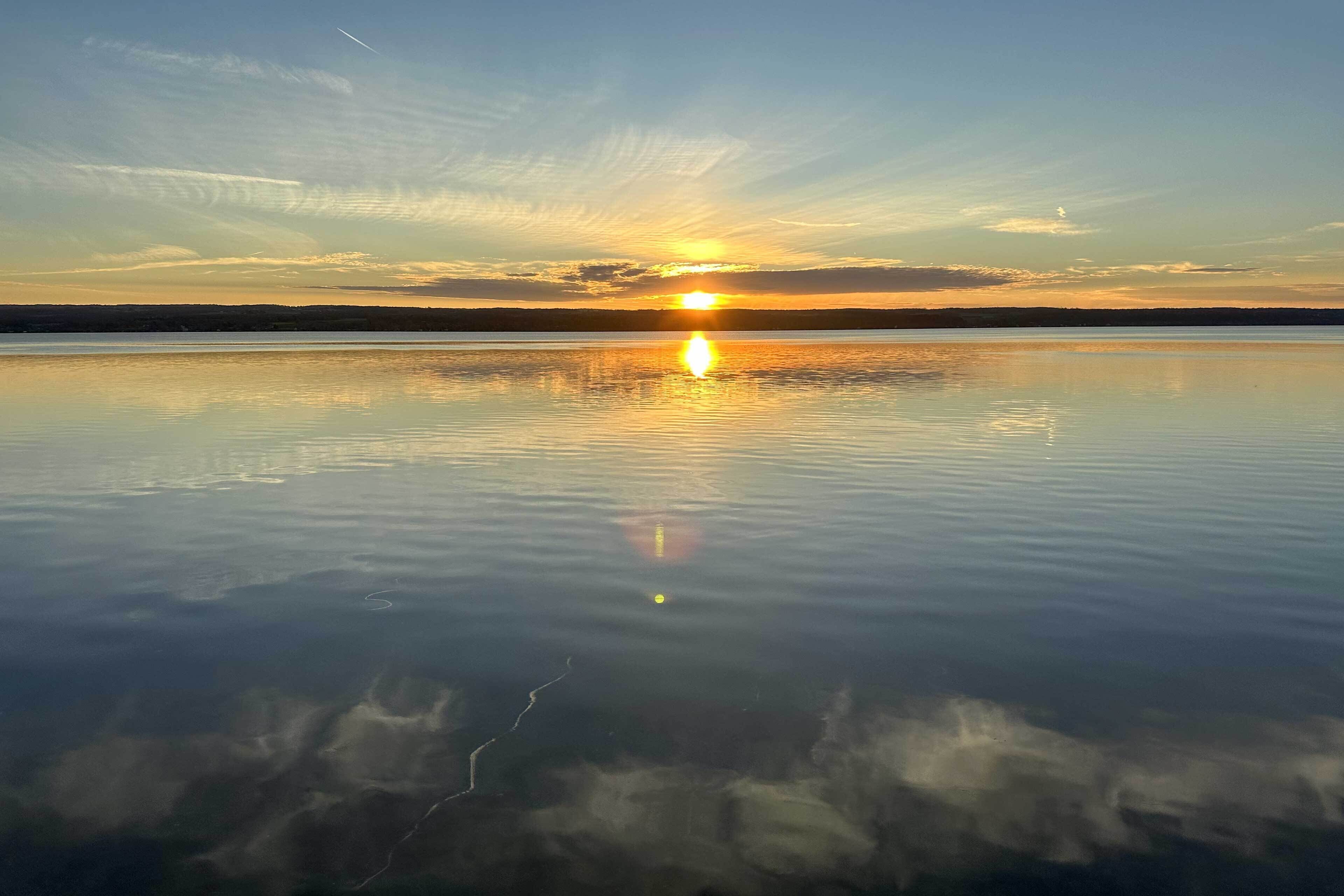 A calm lake at sunset with a clear reflection of the sun on the water's surface.