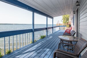 Una terraza de madera con barandilla que da a un cuerpo de agua, con muebles de mimbre y una mesa.