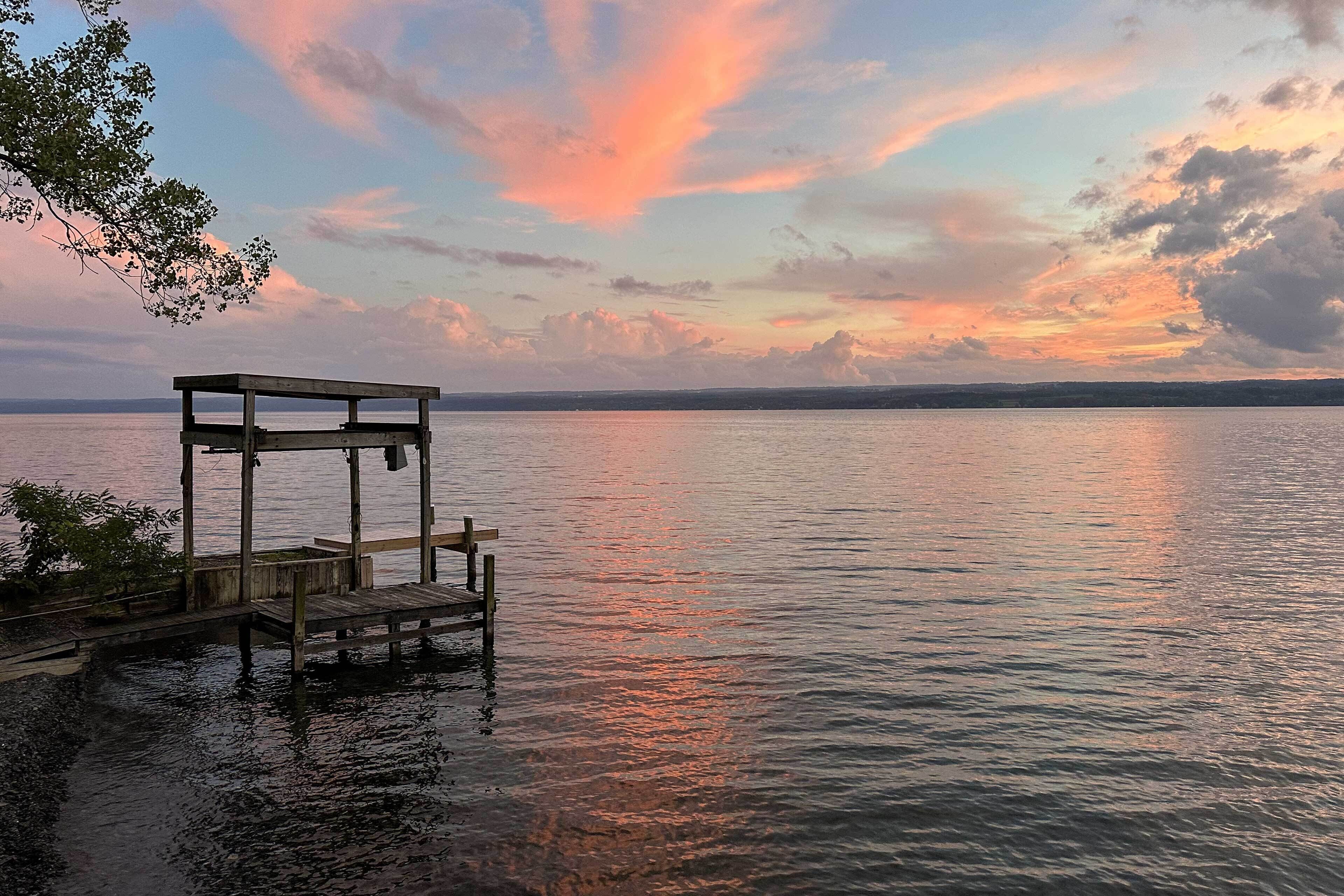Een houten steiger die uitloopt in kalm water, met een zonsondergang op de achtergrond.