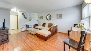 A spacious living room with a wooden floor, a sectional sofa, a dining table with chairs, a staircase, and a large window with blinds. - 3 Mi to Credit Union 1 Amphitheatre: Suburban Stay (Country Club Hills)