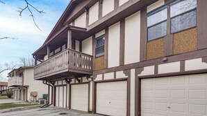 A two-story residential building with a balcony, multiple garage doors, and a visible driveway. - 3 Mi to Credit Union 1 Amphitheatre: Suburban Stay (Country Club Hills)