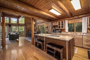 A log cabin interior with a large kitchen, dining area, and a cozy seating space with a view of the outdoors.