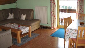 A cozy living room with a brown sofa, a wooden coffee table, and a dining table with chairs. - Comfortably furnished vacation apartment with panoramic views (Arnbruck)