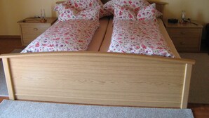 A double bed with floral bedding and two pillows, flanked by wooden nightstands with lamps and a radio. - Comfortably furnished vacation apartment with panoramic views (Arnbruck)