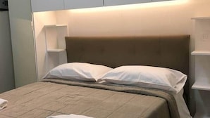A neatly made bed with a beige bedspread and pillows, a folded towel on the bed, and a bedside table with a lamp. - APARTMENT MILAN CENTER PENTHOUSE - PORTA VENEZIA 2DX (Milano)