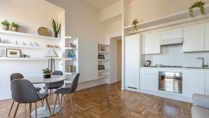 A modern kitchen with white cabinets, a built-in oven, and a coffee machine. There is a dining area with a round table and chairs, and a herringbone-patterned wooden floor. - La Casa al Foro con Vista Mare by Wonderful Italy (Palermo)