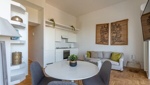 A modern living room with a round white table, grey chairs, a grey sofa with green and yellow cushions, and a white kitchen in the background. - La Casa al Foro con Vista Mare by Wonderful Italy (Palermo)