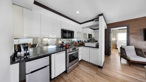 A modern kitchen with white cabinets, a black countertop, stainless steel appliances, and a wooden floor. - Two Bedroom Suites South Beach (Miami Beach)