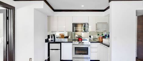 Una cocina moderna con muebles blancos, horno integrado y refrigerador.