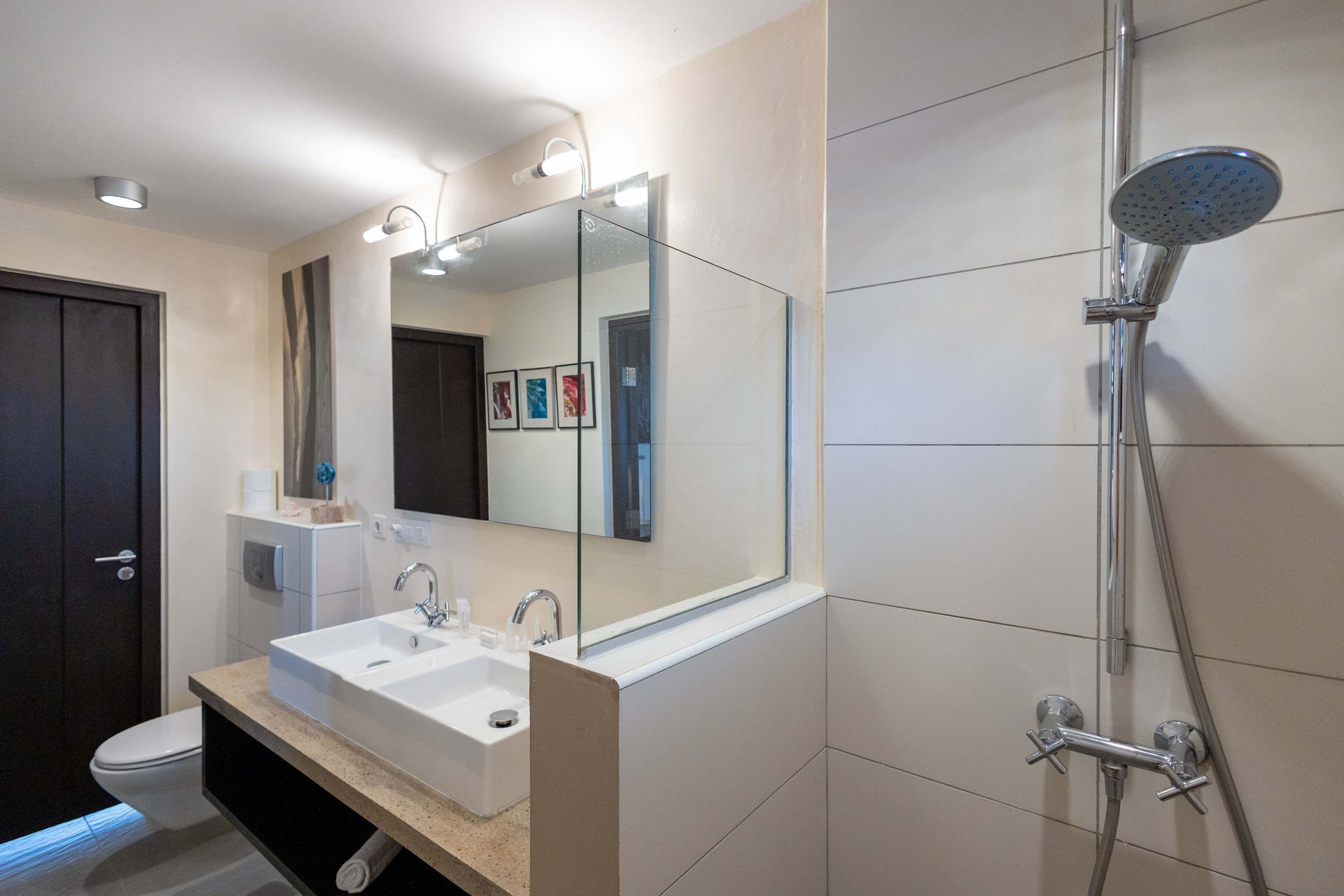 Une salle de bain moderne avec un grand miroir, un lavabo, des toilettes et une douche.